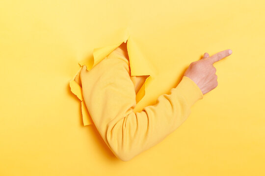Faceless human breaks arm through paper yellow wall indicates on right at blank space, gives advice to buy subscription, suggests to click on link, showing direction. Place for your advertisement