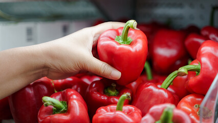 Close up woman hand holding fresh red bell pepper on the shelf at supermarket.