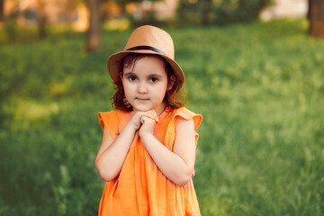 Cute happy little girl in a hat having fun in park meadow or forest. Child look at camera. Picnic on nature