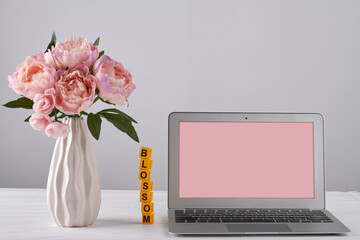 Vase of flowers and laptop with pink screen for copy space. Bouquet of peony flowers and computer on grey background.