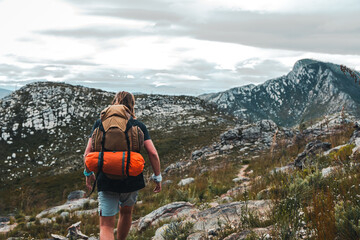 Man hiking towards Valley on a trail with a brown hiking backpack and orange tent on his back In the Witfontein nature reserve in Western cape