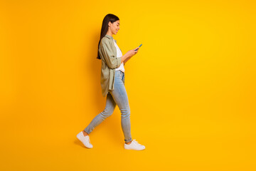 Full body profile portrait of cheerful gorgeous lady walk hold use telephone empty space isolated on yellow color background