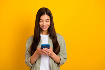 Photo of young pretty good mood girl blogger chatting with boyfriend in smartphone isolated on yellow color background