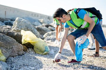 Young ecologic activist man cleaning up the beach, group of volunteers collecting the waste on the...