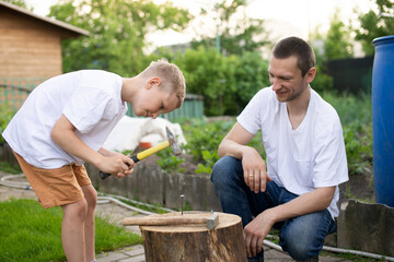 Dad teaches his son to hammer nails into a tree