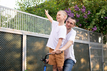 A cute boy in a white T-shirt rides a bike with his dad and laughs.