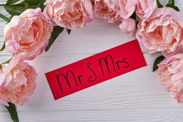 Red paper with mr and ms handwriting on white desk. Frame of pink peony flowers. © DenisProduction.com