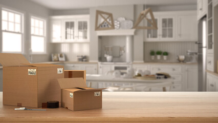 Wooden table, desk or shelf with stack of cardboard boxes over blurred view of scandinavian white kitchen and dining room, modern interior design, moving house concept with copy space