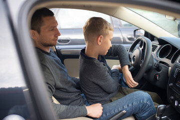 Dad shows his little son how to drive a car