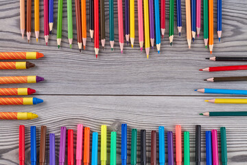 Frame of many colorful pencils and crayons with copy space. Grey wooden desk. Top view flat lay.