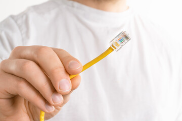 Man's hand holds yellow cable on white background. He is trying to connect computer to the internet...