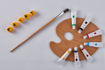 Top view wooden palette with oil tubes. Yellow letter cubes saying word paint.
