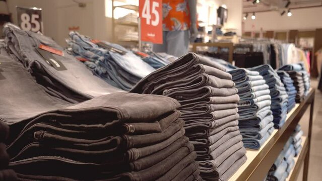 Jeans or denim pants are neatly folded on shelf or window in clothing store. Collection of fashion products in clothing store for sale. Textile industry and business concept.