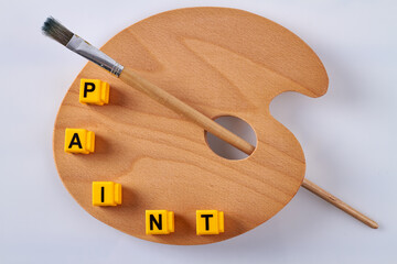 Wooden artist palette with paintbrush on white. Letter cubes arranged in paint word.