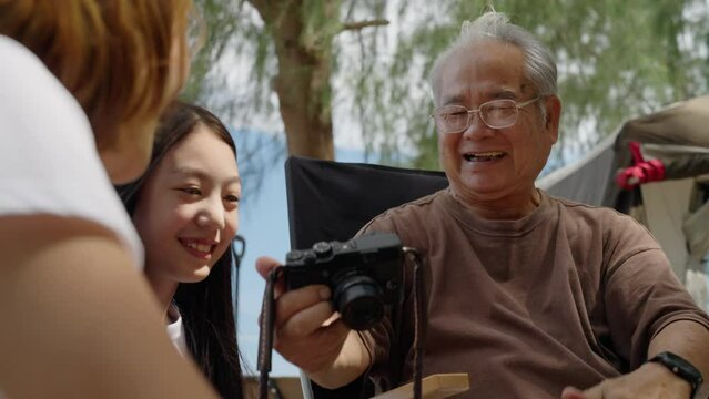 Happy family enjoying with camera on the beach, Big family grandpa daughter and grandchild taking photos together and looking at pictures on digital camera happily, Happy family concept