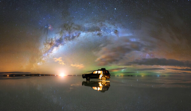 Glowing stars and Milky Way galaxy over salt flat with parked car