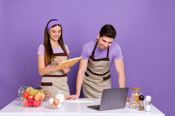 Photo of sweet cheerful boyfriend girlfriend dressed chef outfits learning new recipes gadget isolated purple color background