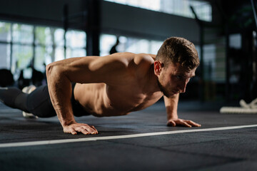 Obraz premium Man doing push ups in a gym. Exhaling and inhaling after push-ups and exercise. Perfect for fitness and workout. Young sports man performs pushups in the gym. The athlete is engaged in fitness