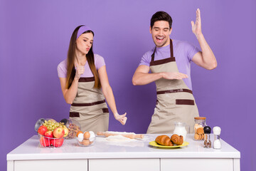 Photo of pretty funny husband wife wear grey aprons backing biscuits dancing isolated violet color background