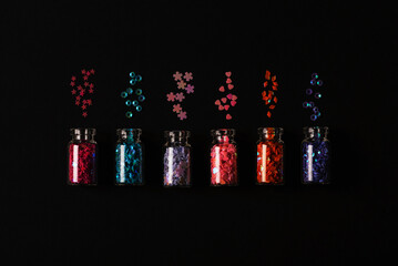 Glass bottles with glitter confetti on black background. Holiday Christmas and New Year concept. Top view, flat lay