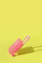 Toy pink suitcase on yellow background with a hard shadow. Copy space. Travel or migration concept