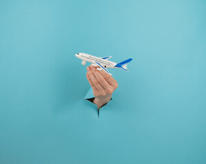 A female hand sticking out of a hole from a blue background holds a model of an airplane. 