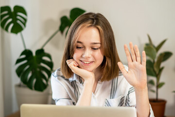 Young smiling woman having video call on laptop at home. Girl greeting friends on a video chat. Female entrepreneur working on laptop at home office. Remote work concept. A business woman is