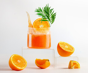 Jar of orange facial peeling mask at podium. Spa setting with orange sugar scrub with tropical green leaf, wooden massage brush and orange fruits. Healthy skin care and beauty treatment. Front view.