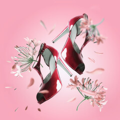 Creative fashion levitation of red high heels with flying flowers and petals at pink background....