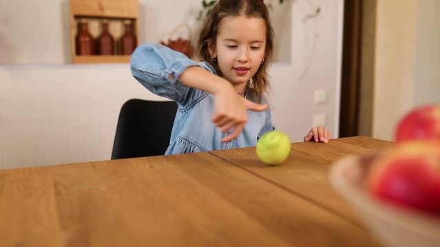 Happy little girl twist the pear, the bowl with variety fruits on table at home, child eating healthy snack, vegetarian nutrition for kids, vitamins for children.