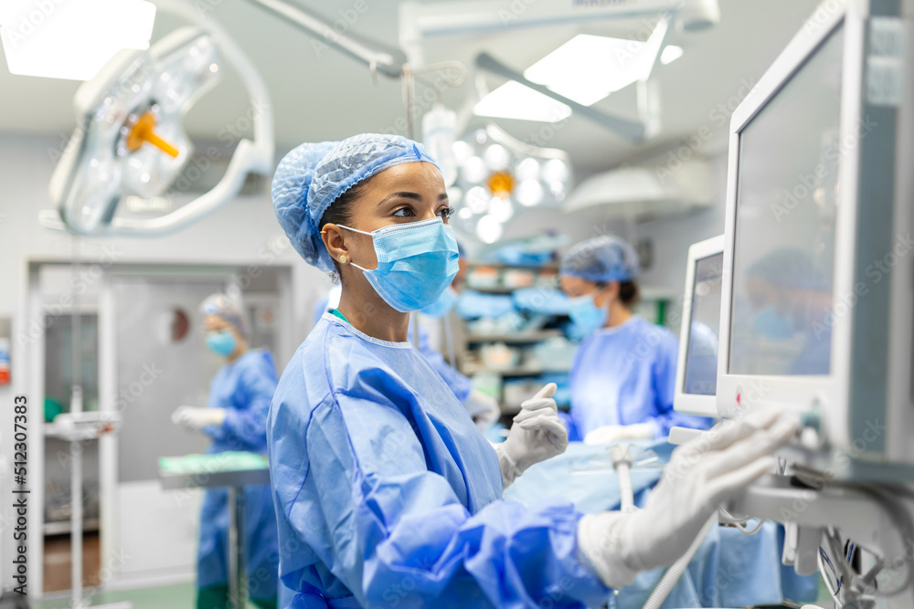 Wall mural Anesthetist Working In Operating Theatre Wearing Protecive Gear checking monitors while sedating patient before surgical procedure in hospital