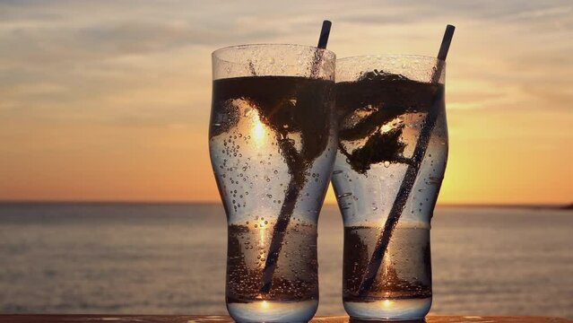 Pair of pint glasses with carbonated water, mint and lemon in Woolacombe Bay at sunset