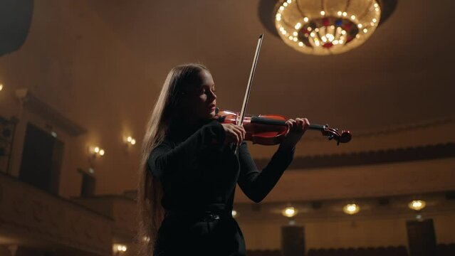 young female musician with fiddle on scene of old opera house, beautiful violinist is playing violin