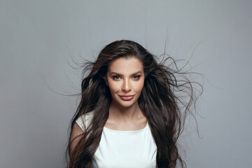 Beautiful young dark-haired woman posing in the studio on a gray background. Wind in female hair....