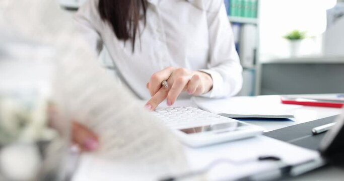Business woman is counting on calculator and holding documents in hands at workplace