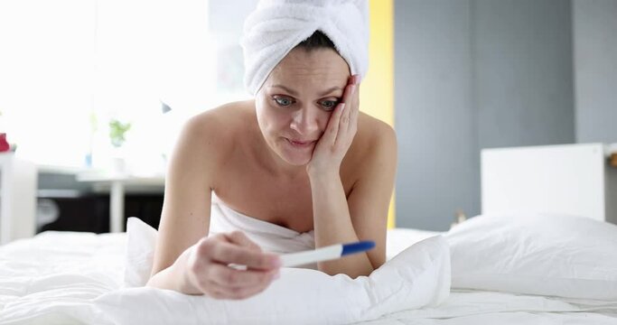 Upset woman holding pregnancy test and crying on bed