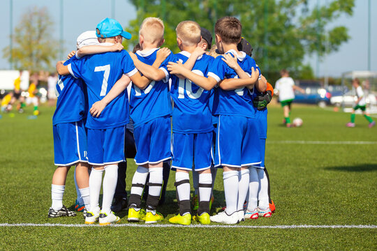 Sporty players huddling in a circle on the field. Motivated youth soccer team cheering on court. Team captain talking to a group of soccer friends. Happy football team in blue soccer uniforms