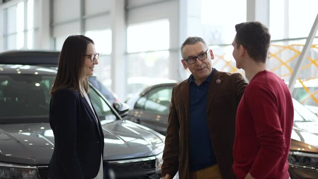 Family people are choosing new car and talking to female agent in modern company spbd. 4k Close view of elderly father, young son examine transport and talk with woman manager, look with smiles and