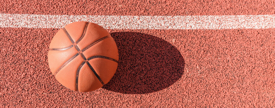 Sports banner.Old orange ball for basketball lying on the rubber sport court.Sport red ground outdoor.Top view,Copy space.Panoramic view.