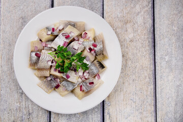 Mediterranean herring fillet served on a plate with chopped onion and parsley on the table