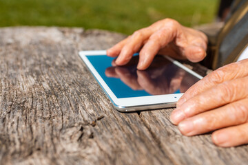 Hands of senior woman holding tablet PC, outdoors in warm summer day.Close up.Selective focus.