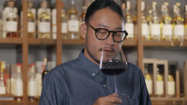 Young Asian sommelier sniffing and tasting newly imported wine and smiling happily after tasting. man hair tie Wine tasting at the restaurant bar at the hotel.