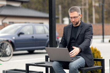 Successful adult handsome man. Works outdoors. Using a laptop.