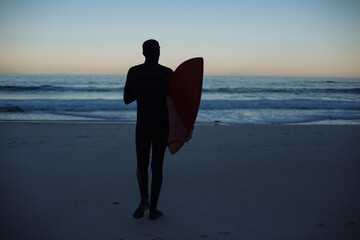Fototapeta na wymiar surfer walking on the beach at sunset