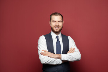 Happy businessman standing with crossed hands and looking at camera on red background