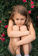 pensive little girl outdoors sitting near a rose bush