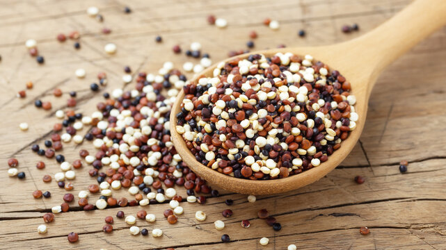 Red, black and white quinoa mixed in wooden spoon