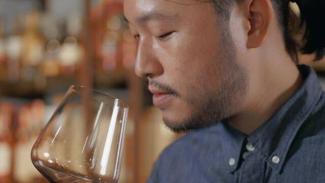 Young Asian sommelier sniffing and tasting newly imported wine and smiling happily after tasting. man hair tie Wine tasting at the restaurant bar at the hotel.