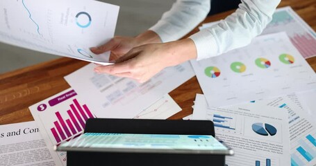 Woman studies data on digital tablet with graphs and documents closeup