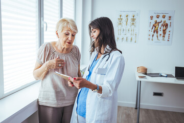 Fototapeta premium Smiling caring young female nurse doctor caretaker assisting happy senior grandma helping old patient in rehabilitation recovery at medical checkup visit, elder people healthcare homecare concept